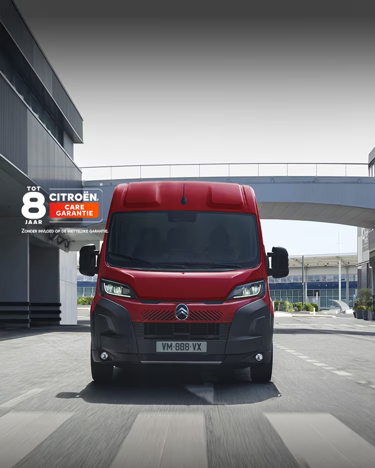 Vooraanzicht van een rode Citroën Jumper-bestelwagen die door een moderne stedelijke omgeving rijdt, waarbij de nadruk ligt op het robuuste ontwerp, de functionaliteit en de opvallende aanwezigheid op de weg.