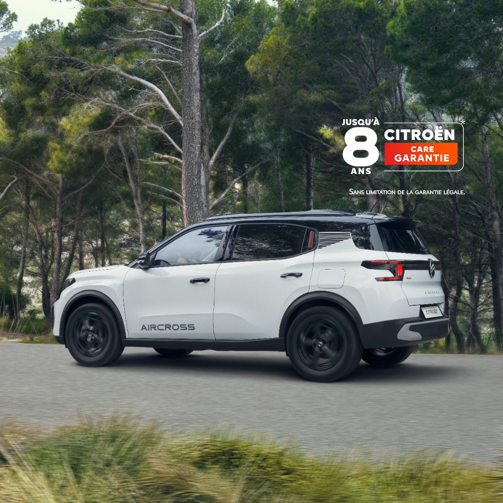 Vue trois-quarts arrière bord de mer en conduite sur une route forestière du SUV électrique Citroën ë-C3 Aircross mettant en valeur un design primé et une couverture de 8 ans pour une mobilité abordable.