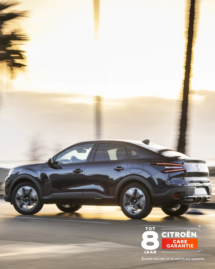 Citroën ë-C4 X rijdt bij zonsondergang over een kustweg met het 8-jaars dekking-badge van de Citroën