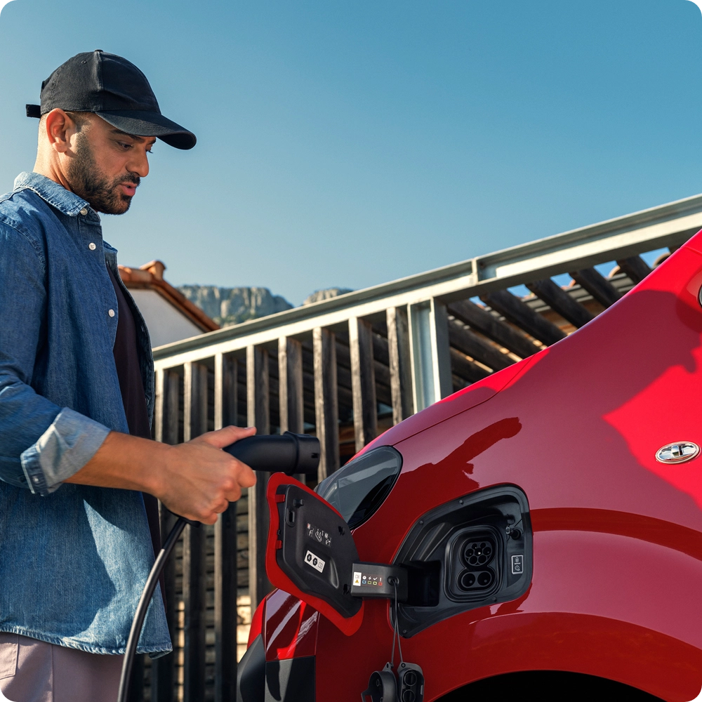 Side exterior view of a red Citroën ë‑Jumpy being charged while a smartphone is used, showing connected services, trip planning and easy electric journey management.