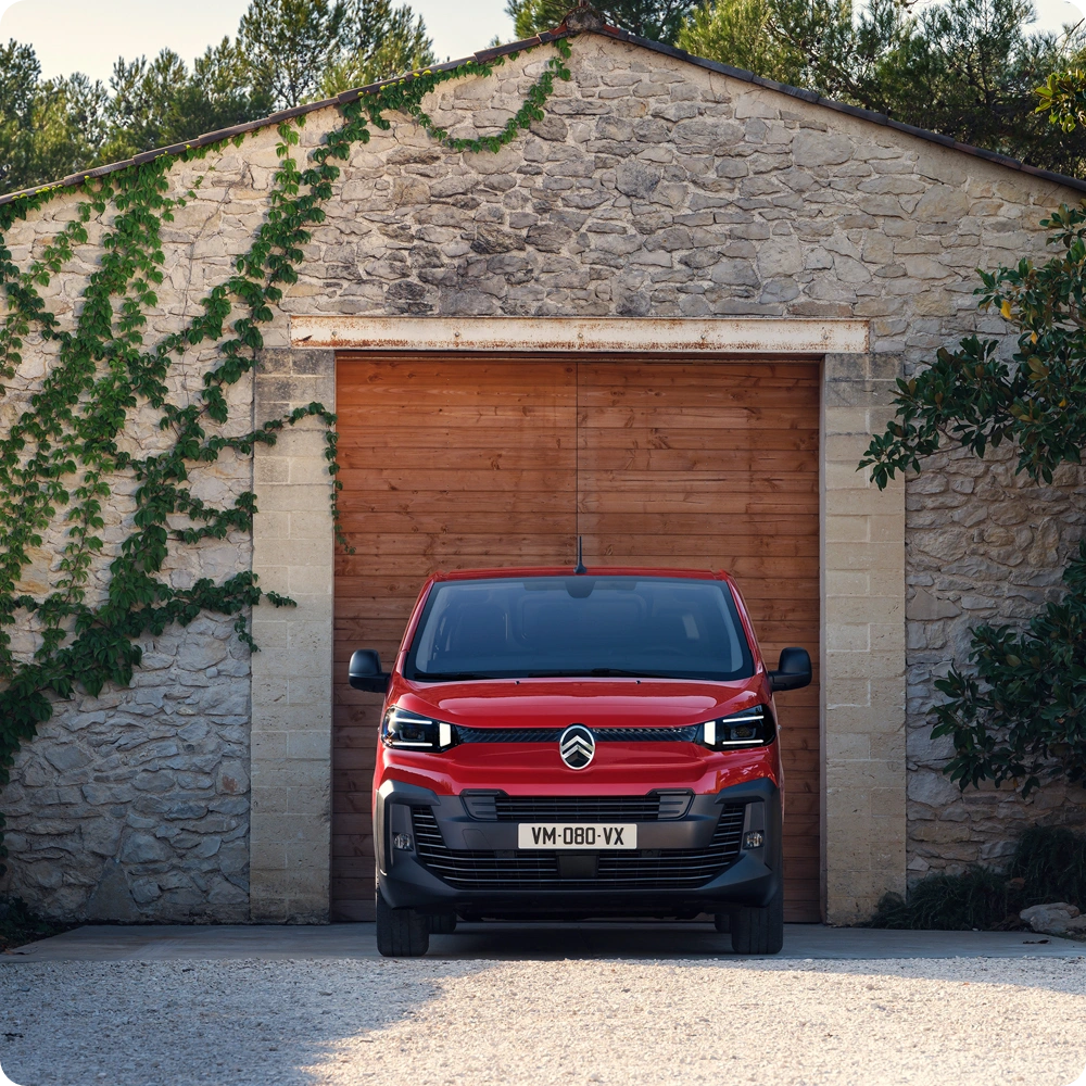 Front exterior view of a red Citroën ë-Jumpy parked in front of a building, showing professional design, robustness, practicality and confident presence.