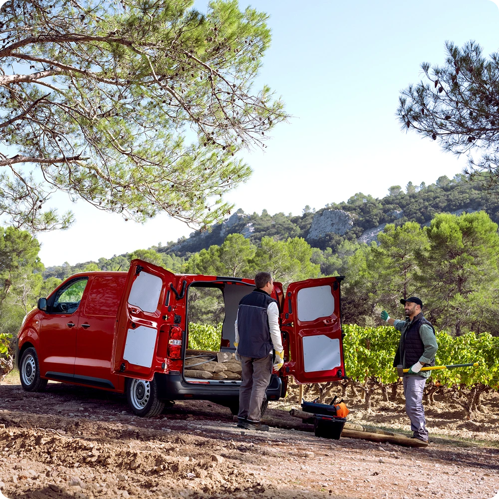 Rear three‑quarter exterior view of a red Citroën ë-Jumpy with rear doors open during loading, showing versatile cargo space, practical access and suitability for professional use.