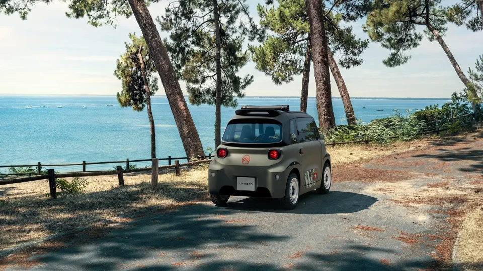Vue arrière trois-quarts de Citroën Ami Outdoor en bord de mer présentant un véhicule urbain électrique avec toit ouvert pour les déplacements de loisirs