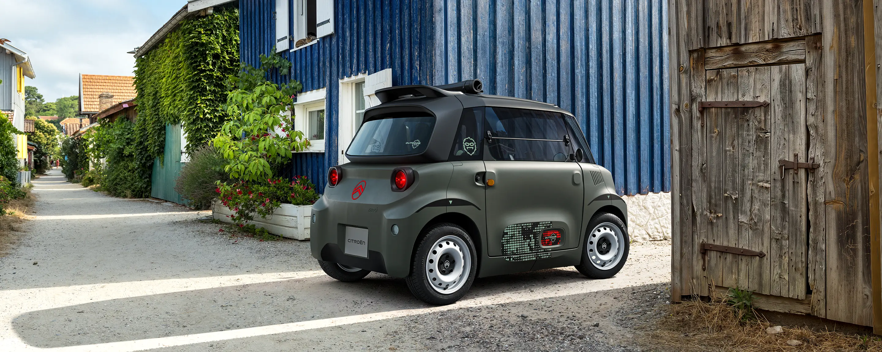 Vue avant trois-quarts de Citroën Ami Outdoor avec phares LED présentant un véhicule urbain électrique compact dans un village côtier