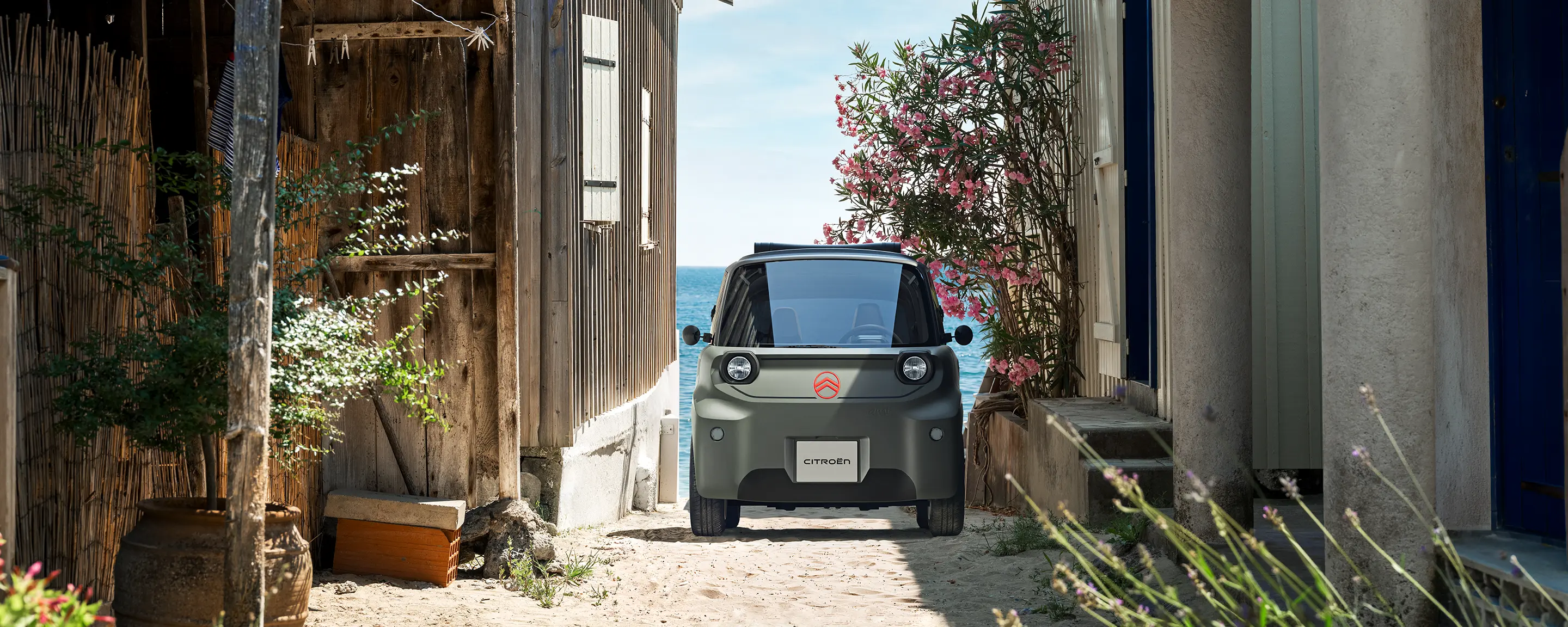 Vue avant de Citroën Ami Outdoor avec phares LED présentant un véhicule urbain électrique compact circulant dans une ruelle étroite du littoral
