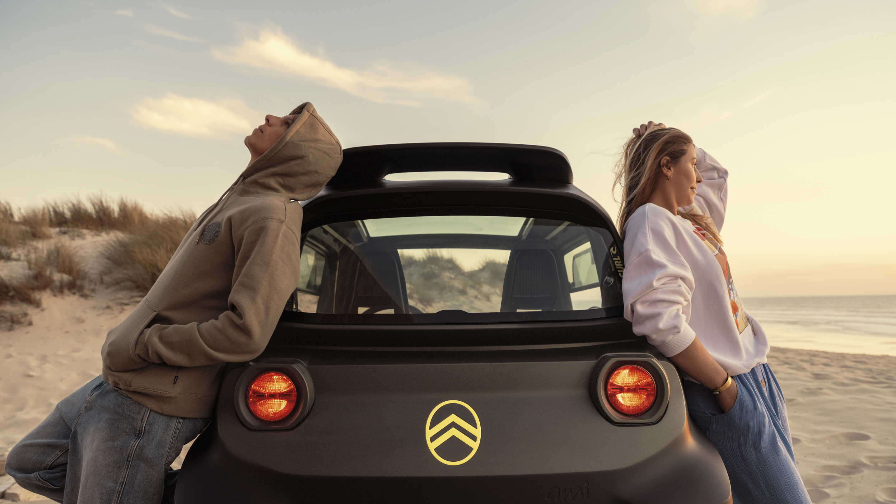 Lifestyle achteraanzicht bij zonsondergang van de Citroën Ami x Rip Curl elektrische wagen zonder rijbewijs, Citroën Ami staat voor ontspannen vrijheid in stedelijke elektrische mobiliteit
