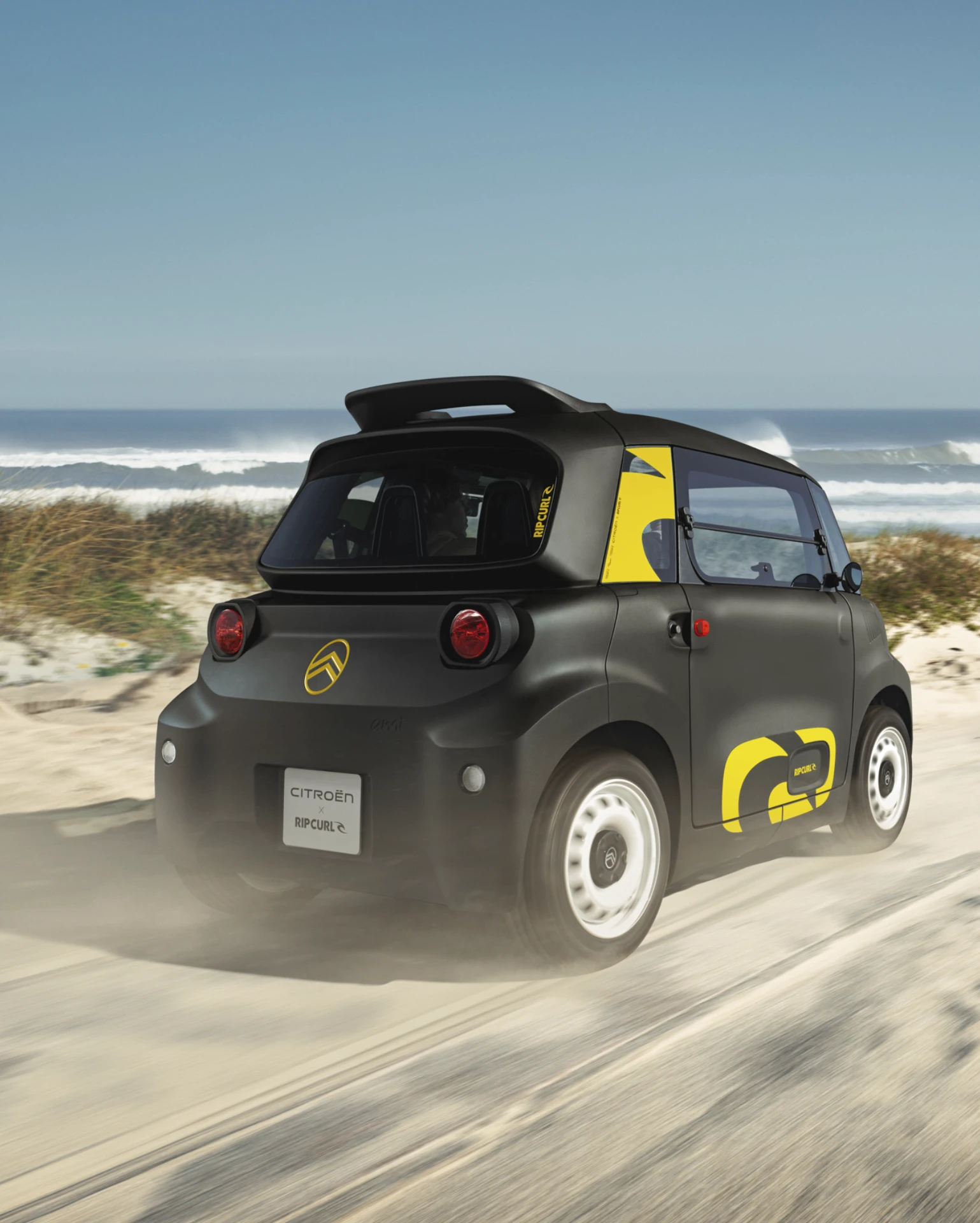 Driekwart achteraanzicht tijdens rijden van de Citroën Ami x Rip Curl elektrische wagen zonder rijbewijs, Citroën Ami staat voor rijplezier in stedelijke elektrische mobiliteit