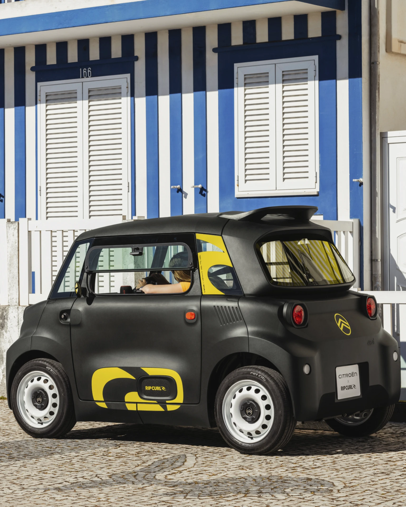 Achterzijde zijaanzicht op straat van de Citroën Ami x Rip Curl elektrische wagen zonder rijbewijs, Citroën Ami staat voor veiligheid op vier wielen in stedelijke elektrische mobiliteit