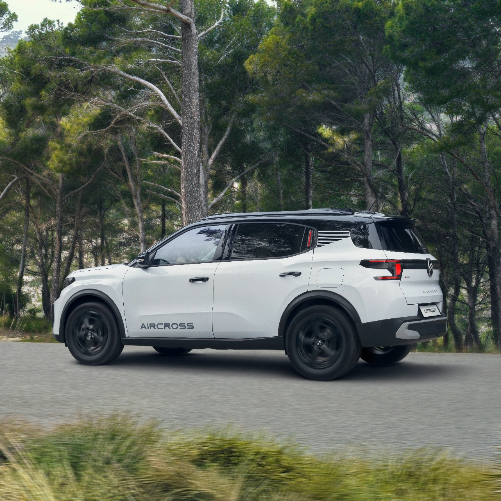 Vue trois-quarts arrière bord de mer en conduite sur une route forestière du SUV électrique Citroën ë-C3 Aircross mettant en valeur un design primé et une couverture de 8 ans pour une mobilité abordable.