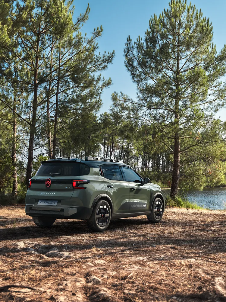 Driekwartachteraanzicht van de Citroën ë-C3 Aircross met LED-lichtsignatuur en Advanced Comfort, een gezins-SUV op een bosweg