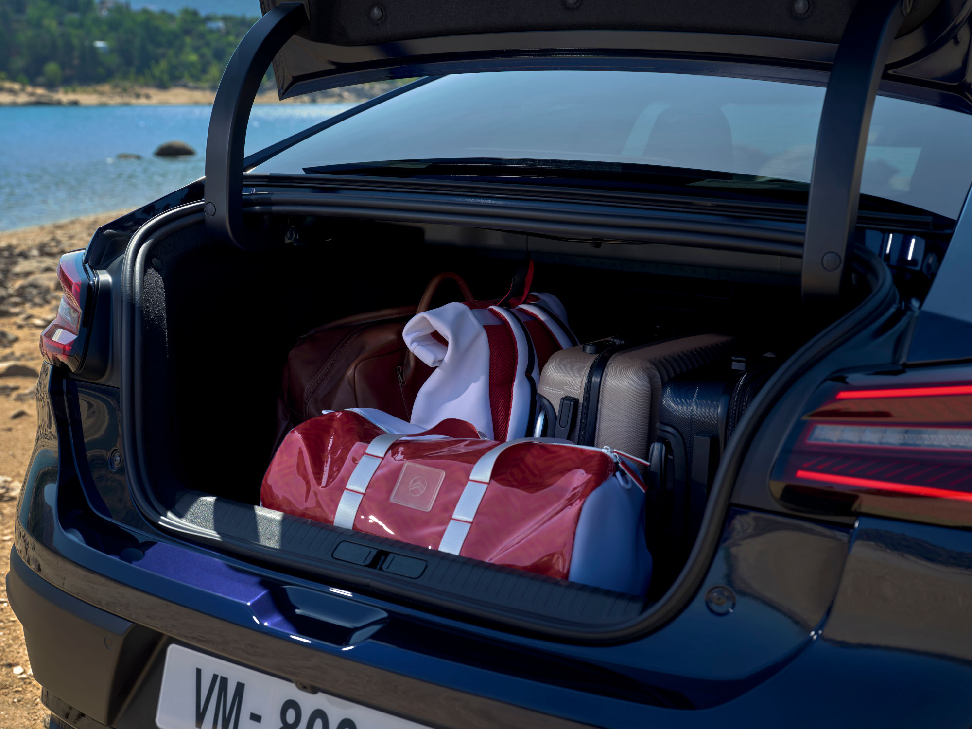 Coffre ouvert de la Citroën C4 X chargé de sacs de voyage à côté d’un emplacement au bord d’un lac