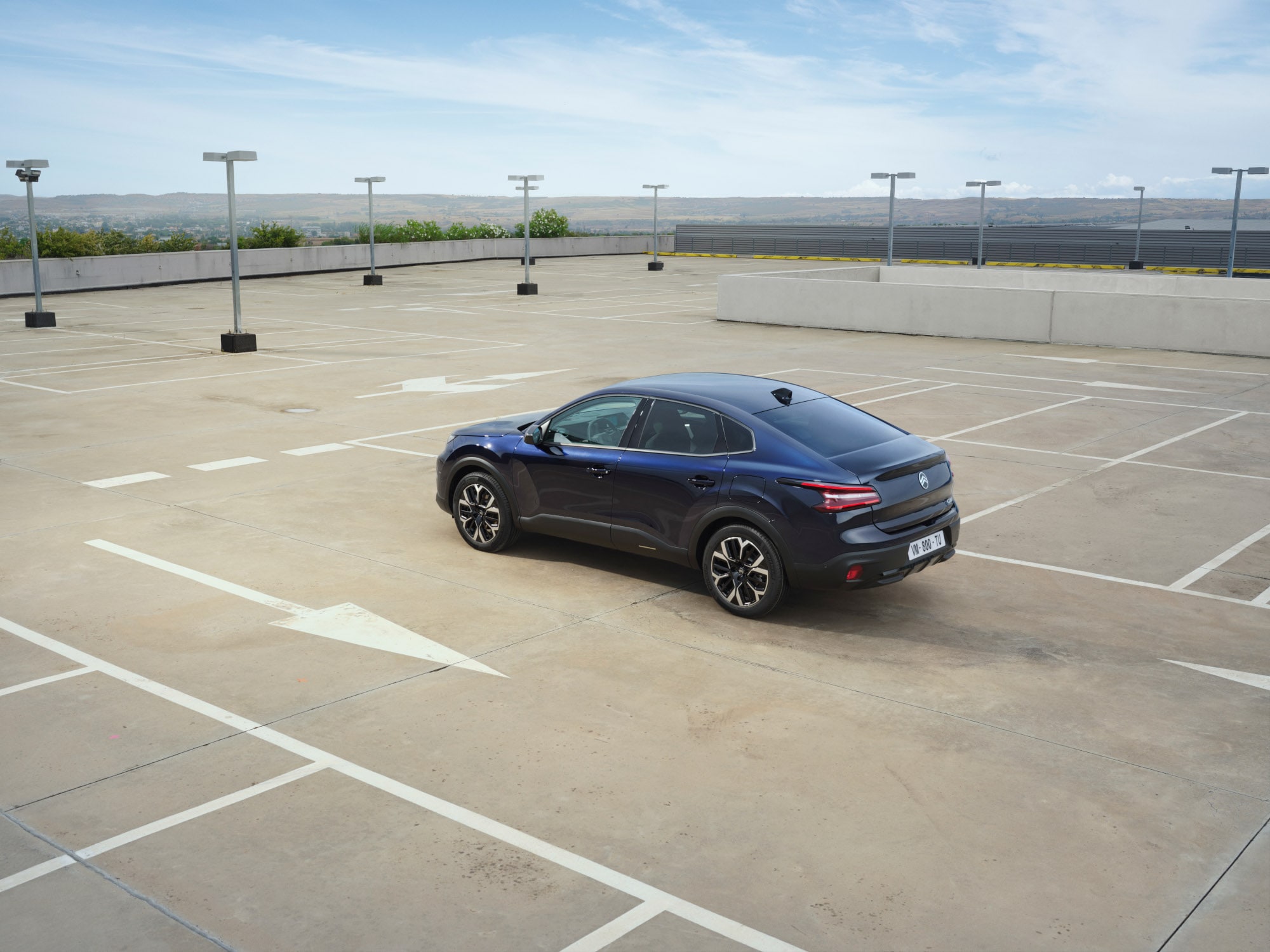 Vue arrière trois quarts de la Citroën C4 X sur un parking ouvert sur le toit, mettant en valeur des lignes fastback élégantes pour une mobilité abordable