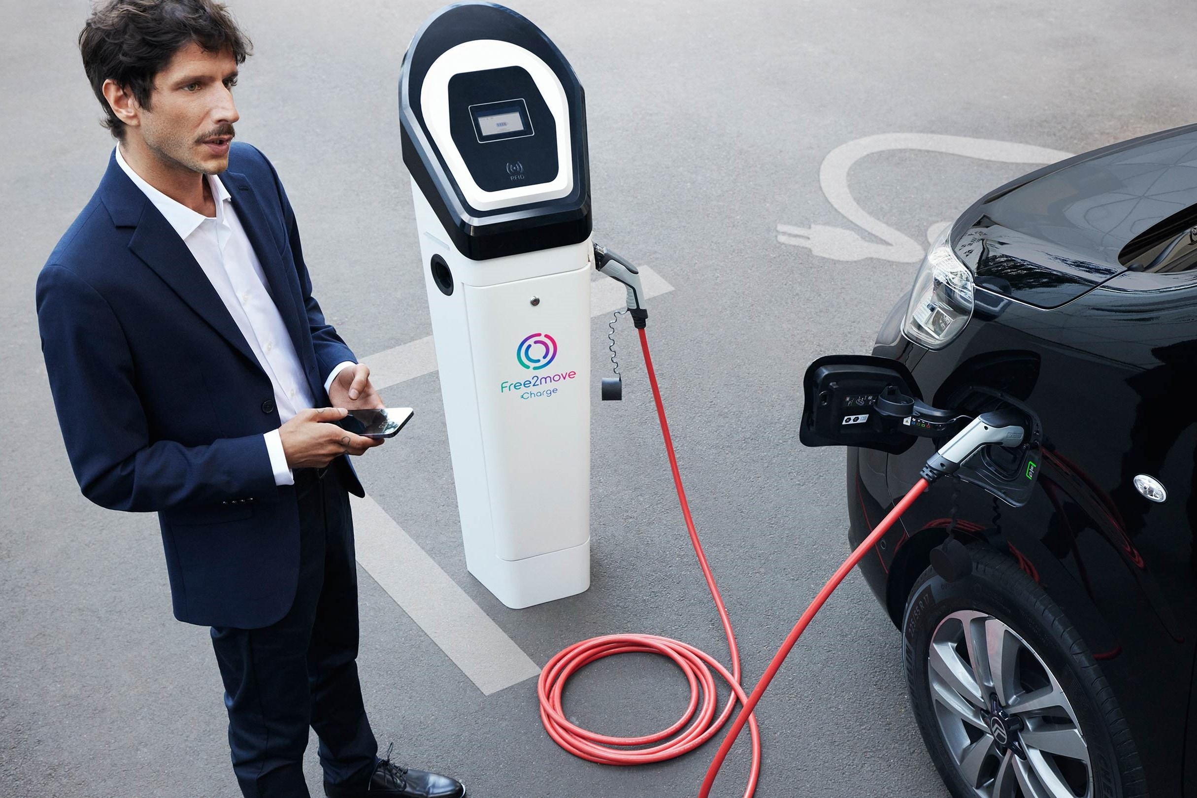 Véhicule électrique en charge à une borne publique pendant l'utilisation d'une application smartphone pour gérer la charge avec Free2move Charge